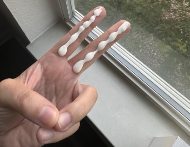 An adult hand making the "peace sign" the number two with two fingers, with a line of sunscreen the length of the two fingers.